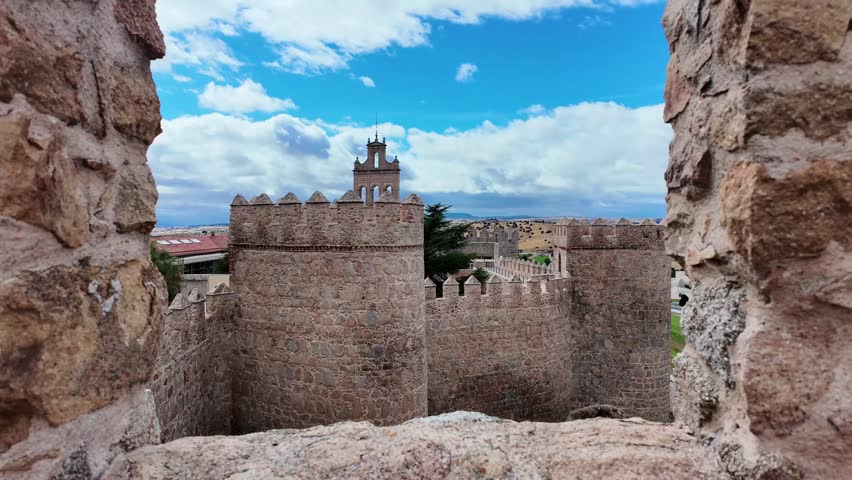 Wide view of the historic medieval city walls of Ávila Spain stretching across grassy hill under a dramatic cloudy sky. One of the best-preserved fortified cities in Europe and a UNESCO heritage site