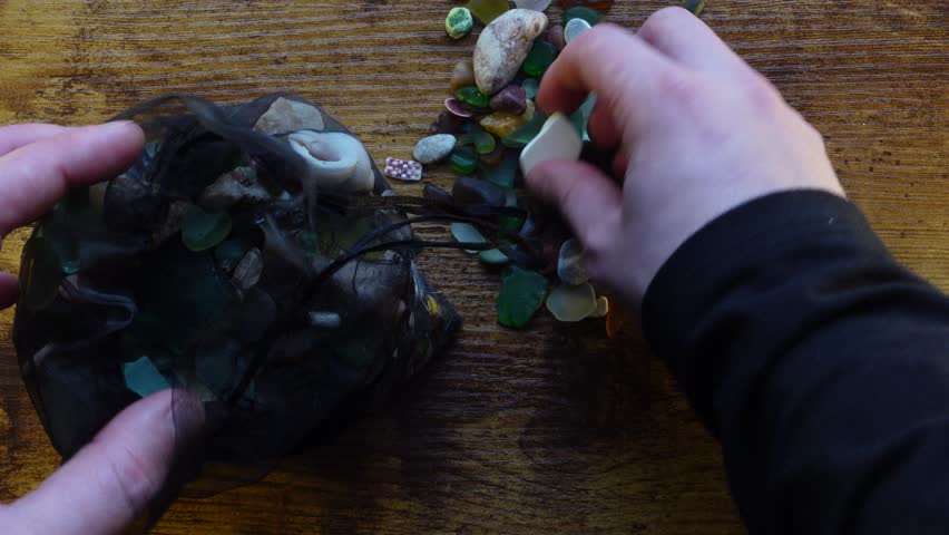 Hands picking and examining sea glass, shells and pebbles scattered on the table