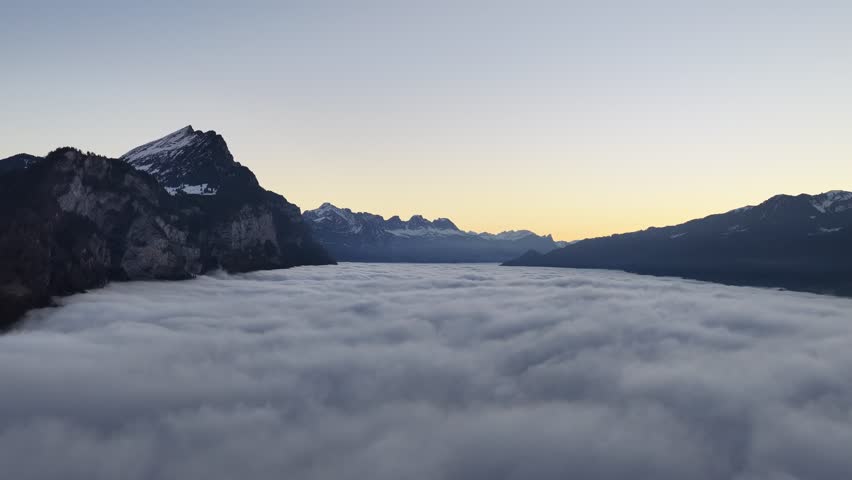 Dramatic aerial view of Swiss peaks floating over a dense sea of fog. The hidden Walensee valley creates a mystical, high-altitude winter landscape near Walenstadt.