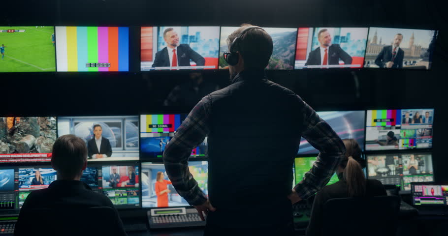 Backstage TV Station Production Control Room Captures Technicians and Operators Directing Live News Broadcasting, Switching Anchor, Weather and Sport Channel Feeds Across Monitor Walls and Consoles.