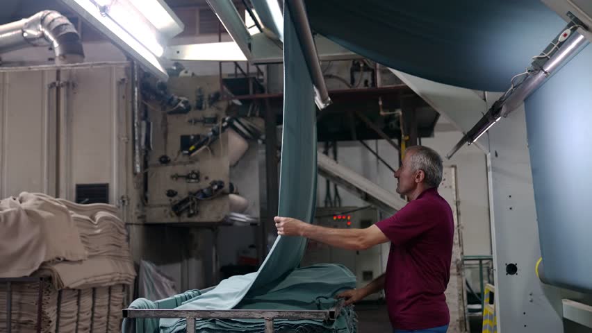 Professional industrial footage reflecting human labor, work discipline and years of experience. Portrait of an experienced textile worker standing in a factory production area.