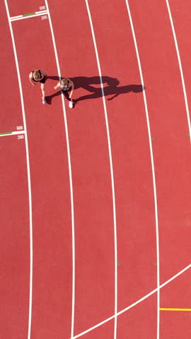 Birds eye view of two female athletes jogging on a red athletic track during a sunny day. Ideal for sports, fitness, and healthy lifestyle content.