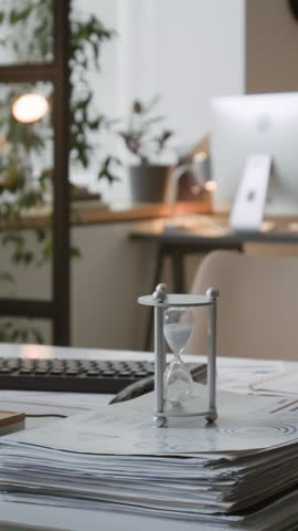 Vertical close up shot of office desk with documents, hourglass and leafy plants in productive workspace