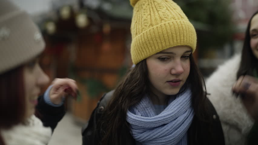 Three playful teenage girls enjoy a fun moment outdoors during winter, laughing together. Friends share a lighthearted interaction, pulling a hat over one girl
