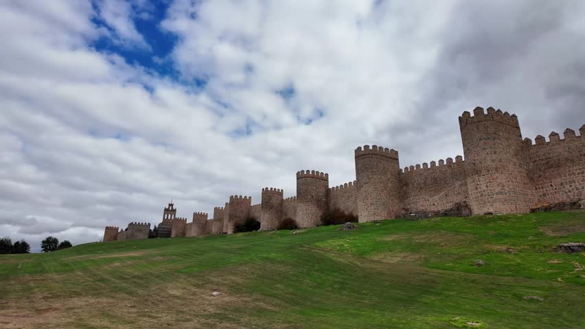 Wide view of the historic medieval city walls of Ávila Spain stretching across grassy hill under a dramatic cloudy sky, one of the best-preserved fortified cities in Europe and a UNESCO heritage site