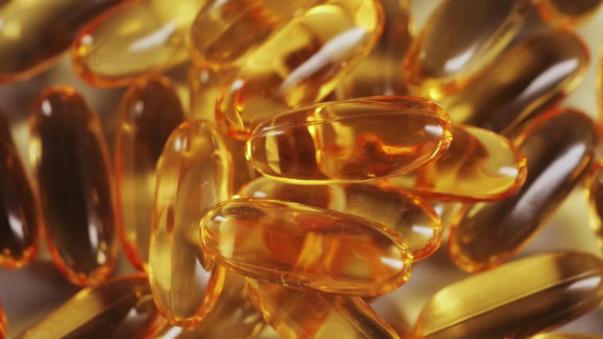 A close-up of Omega-3 capsules, clear, golden, and glossy. The soft gel capsules are filled with fish oil on a surface. Health and daily wellness support.