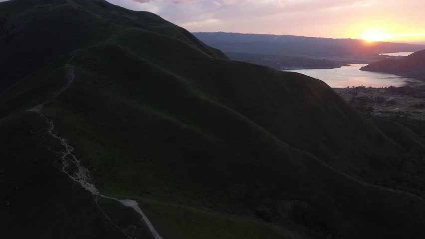 Spectacular aerial view of the sun slowly rising above Bukit Holbung, bathing the rolling highland landscape in warm golden light and creating a peaceful, unforgettable morning scene in North Sumatra.