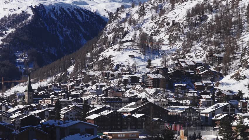 Aerial glide across the alpine village of Zermatt showing chalets, hotels, church steeple and ski lifts beneath the iconic Matterhorn in the Swiss Alps.