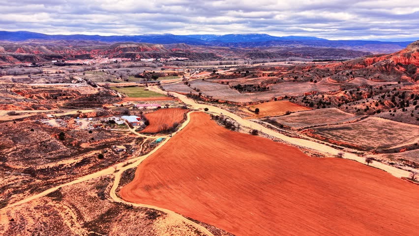 High angle perspective of cultivated red soil farmland with hills and a village in the background. Aerial view of red agricultural fields and distant town.