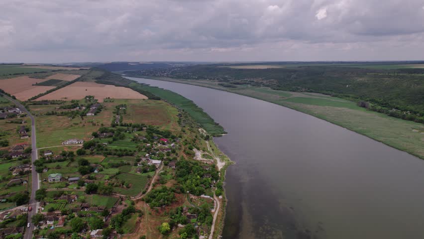 Overcast Sky Over Tranquil River Village, Peaceful Village Nestled In Rolling Hills By Winding River