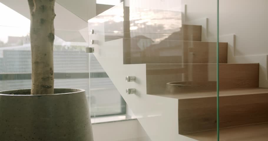 Modern and minimalist staircase with wooden steps and a glass balustrade, revealing a clean, bright, and luxurious home interior design with a large potted plant next to a window