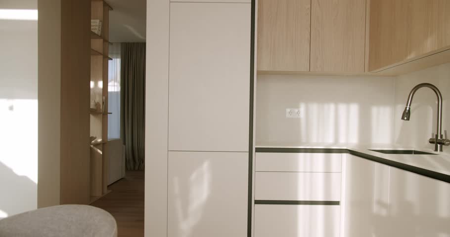 Bright and clean contemporary kitchen interior featuring sleek white cabinets, wooden elements, and a modern faucet, with sunlight creating beautiful shadows and reflections across the surfaces