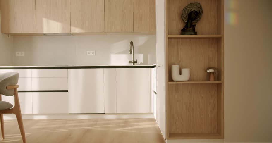 Modern kitchen interior with wooden cabinets and laminate flooring basking in the warm morning sunlight, showcasing a clean, minimalist design with elegant decorative elements on the shelves