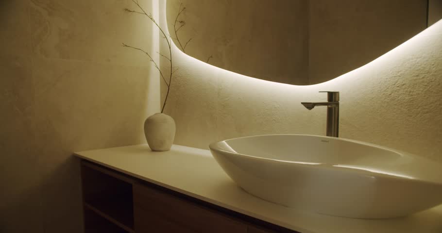 Luxurious contemporary bathroom with white vessel sink on wooden vanity, sleek faucet and backlit modern mirror creating a warm, minimalist spa-like atmosphere in home interior