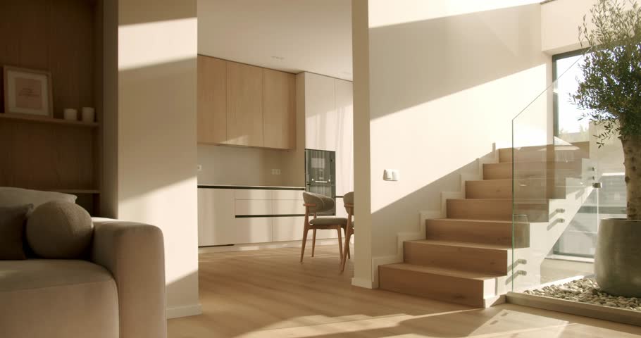 Warm sunlight and shadows moving across the floor and walls of a modern and stylish home interior, showing a living room, kitchen, and wooden staircase in a peaceful time-lapse style