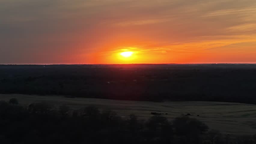 Aerial drone slide left over cattle pasture with reflective pond during vivid sunset in rural Oklahoma