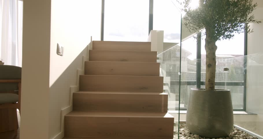 Luxurious contemporary house featuring a minimalist wooden staircase next to a large glass window, with bright natural light creating beautiful highlights and shadows in a serene and elegant space