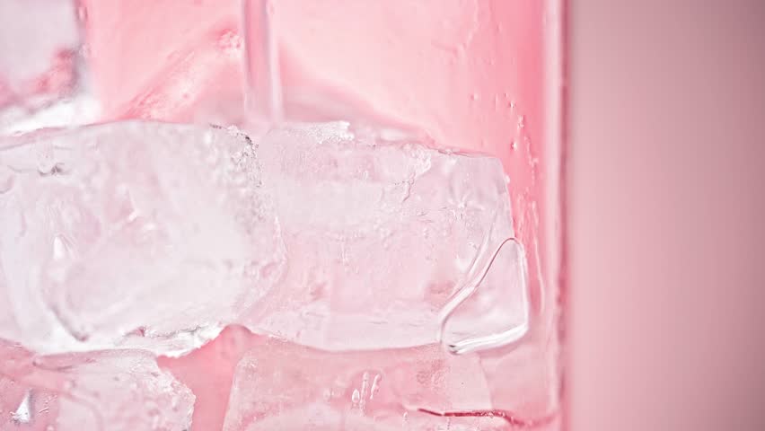 Macro Close-up of Pink Liquid Pouring into a Glass with Ice Cubes on Pink Background, Refreshing Summer Drink Advertising