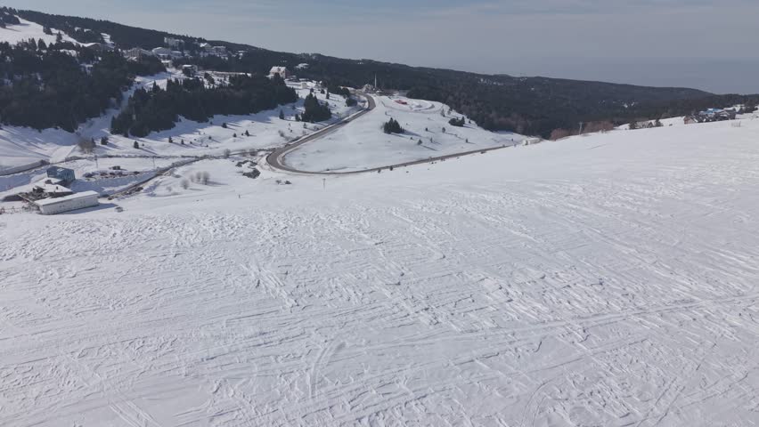 Aerial forward tracking shot over a snow-covered ski resort and mountain road at Uludag