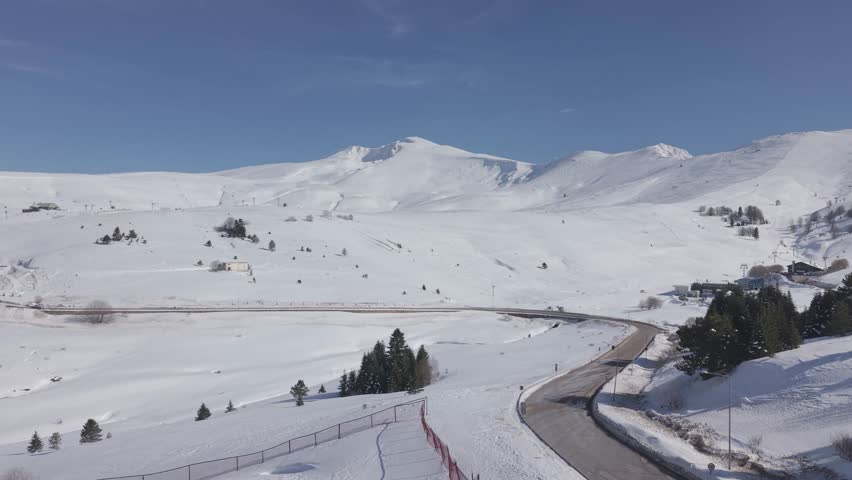 Aerial forward tracking shot over a snow-covered ski resort and mountain road at Uludag