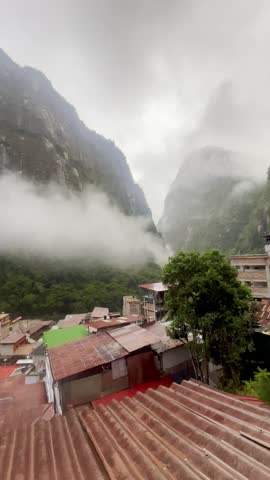 Wide panorama of Aguas Calientes town – Machu Picchu Pueblo – nestled in a steep Andean valley below Machu Picchu, with colorful buildings along the river. Filmed in Peru.