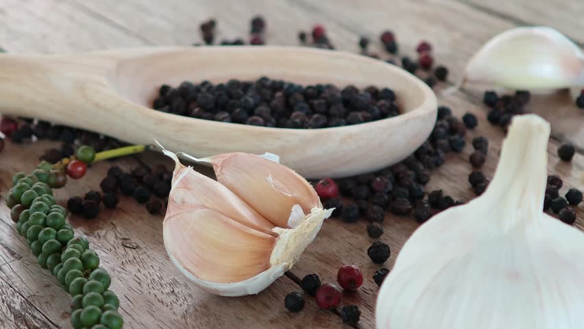 Black peppercorns, green peppercorns, red peppercorns, and garlic are placed on the wooden floor.