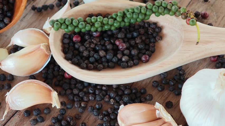 Black peppercorns, green peppercorns, red peppercorns, and garlic are placed on the wooden floor.