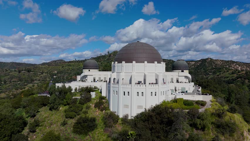 Griffith Observatory aerial drone rising above observatory with Los Angeles hills and blue sky clouds