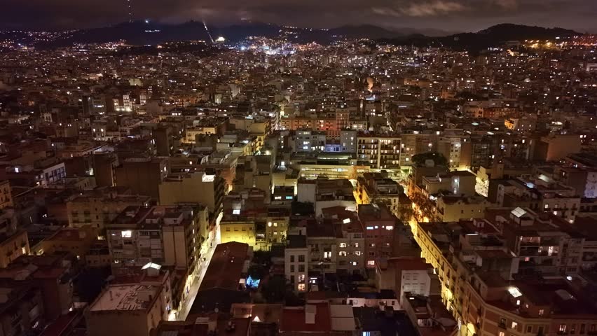 Night drone panning of Barcelona city lights spreading across urban landscape, Barcelona, Spain