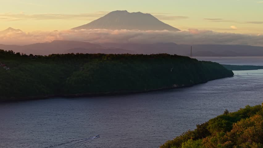Warm sunset light illuminates Mount Agung towering above clouds and Bali coastline