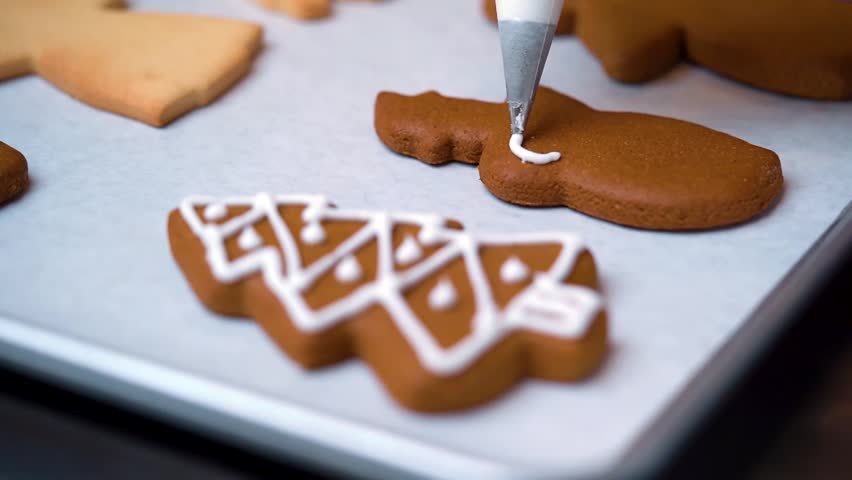 Close-up video of decorating a snowman-shaped Christmas cookie using white icing under natural lighting, capturing the festive holiday baking process.