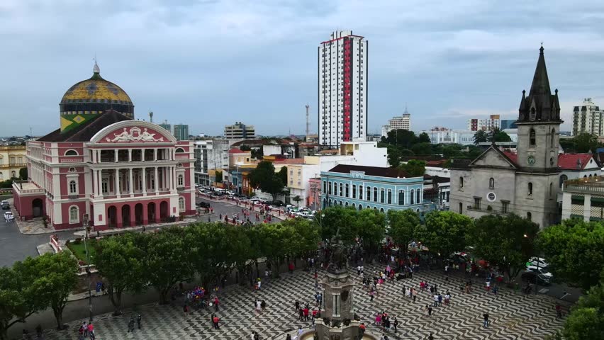 Main square at Teatro Amazonas in Manaus, Brazil. Large crowds of people fill the area during a cloudy afternoon. Static aerial next to historic fountain in 4K.