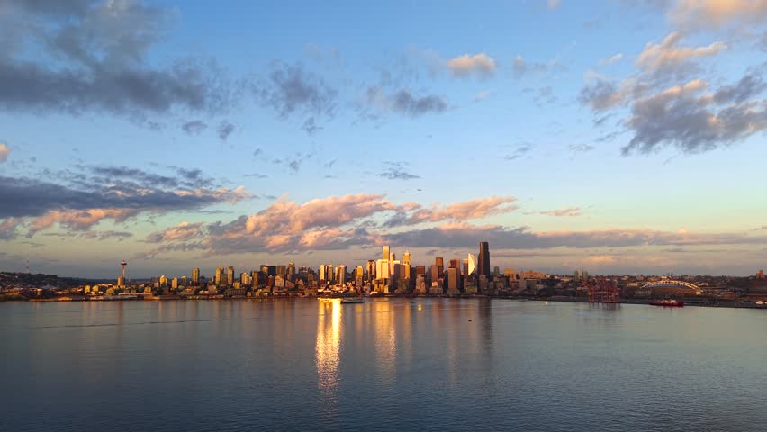 Panoramic view of the downtown Seattle skyline with golden light and dramatic sky reflecting on the water.