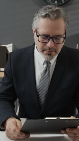 Vertical shot of middle-aged formally dressed personnel manager giving resume back to young applicant asking him to sign it