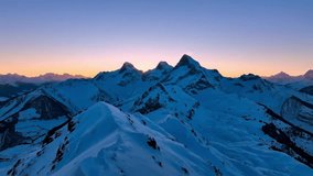 This video captures a high-altitude mountain range during sunrise. The visual documents snow-capped jagged peaks and deep valleys illuminated by low-angle sunlight. The composition illustrates atmospheric lens flares and the golden light transition across the alpine terrain, documenting mountain geomorphology and light scattering in a high-resolution 4K format for environmental media. - Powered by Shutterstock - Get 15% off with code: PIKWIZARD15