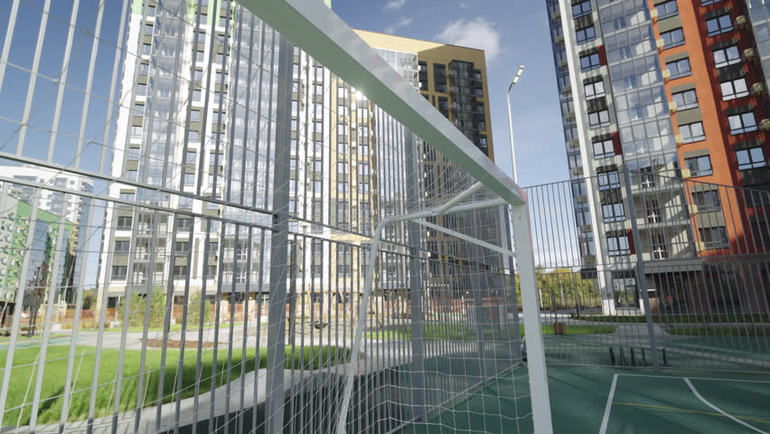 Football goals stand near fence of sports field in landscaped residential territory. Athletic space integrated into urban environment