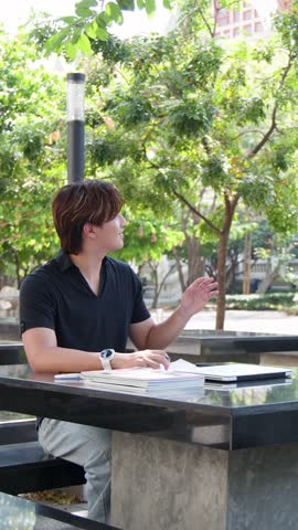 Three Asian students greet each other and discuss coursework at an outdoor campus stone table