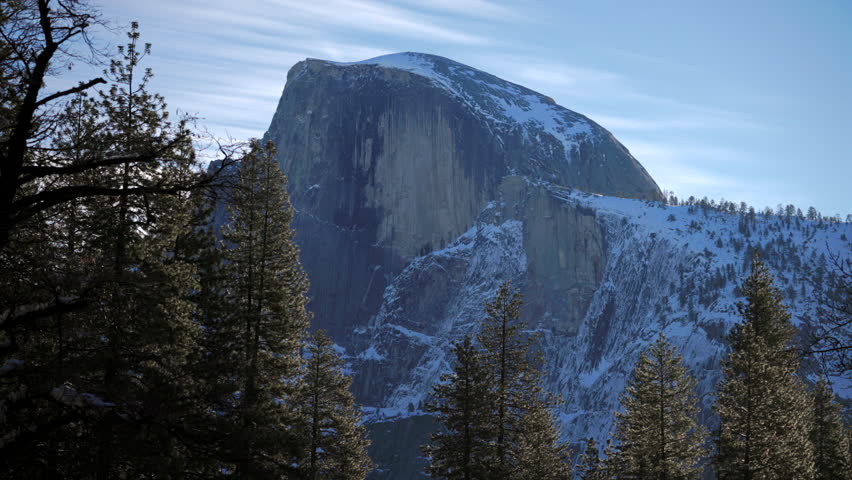 Snowcapped half dome in Yosemite National Park framed by pines granite monolith rises above timbered ridgeline crisp sky and distant snowy slopes convey solitude, winter landscape