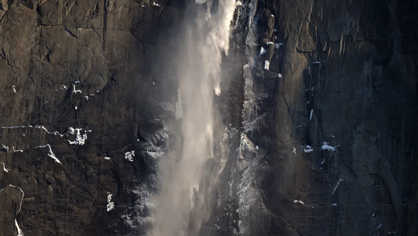 Sunlit waterfalls with gentle spray. Warm sunlight illuminating granite with mist and droplets. Cinematic glow highlights intimate vertical scene with falling vapor. Yosemite National Park