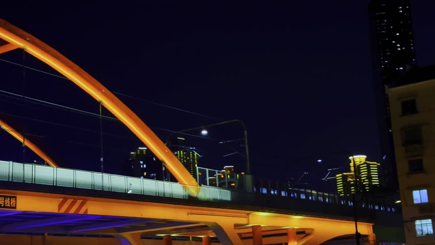 Night view of a Shanghai metro train passing over a bright yellow arched bridge. Modern urban transportation with skyscrapers and city lights under a deep blue night sky.
