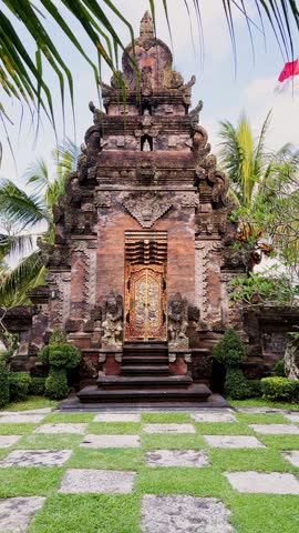 Vertical scene of a historic Balinese Hindu temple entrance framed by palm trees highlighting traditional religious architecture on the island of Bali Indonesia.