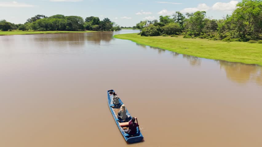 Three people enjoying a wildlife safari on a traditional canoe in a vast river landscape