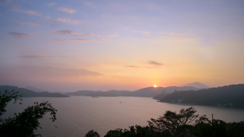 A breathtaking sunset view over Sun Moon Lake in Nantou, Taiwan, featuring calm water, distant mountains, and a soft colorful sky.
