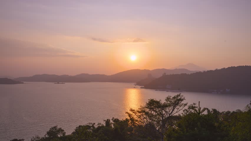 A breathtaking sunset view over Sun Moon Lake in Nantou, Taiwan, featuring rolling mountains, calm water, and a warm golden sky.