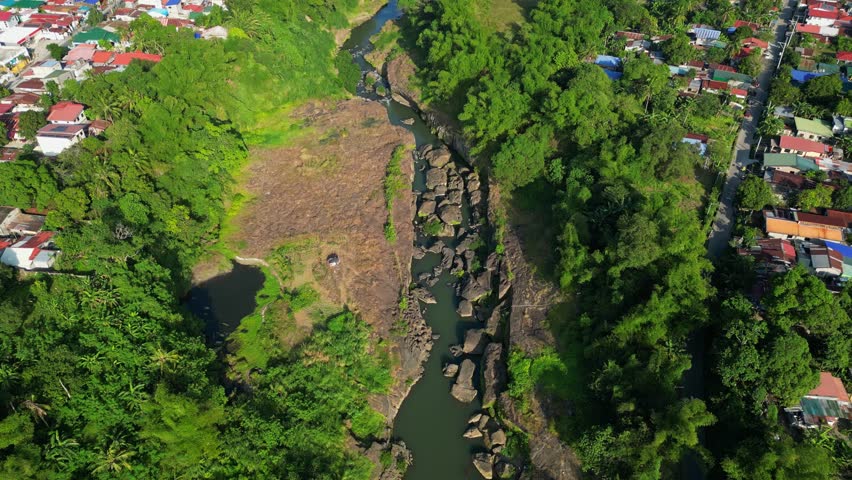 Forward drone movement above rocky river revealing nearby houses, rice paddies, and highway road in Bucal Tulay Maragondon Cavite Philippines