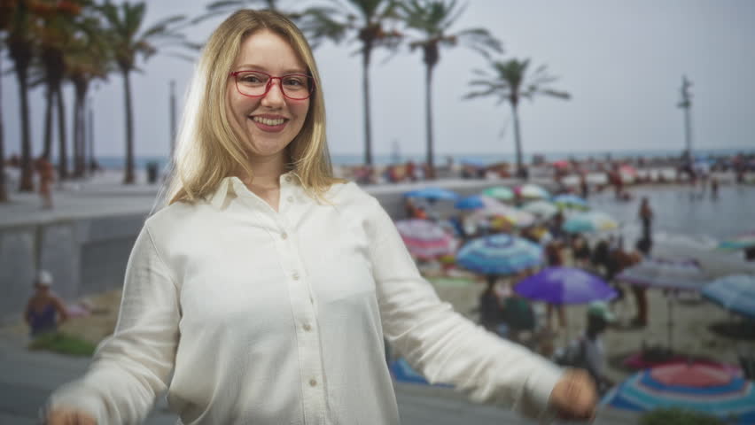Woman pointing thumbs to chest on crowded street boardwalk by beach, wearing white shirt and red glasses; playful joy.