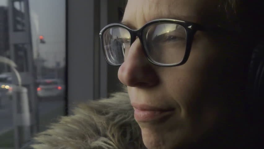 A static shot captures a person wearing glasses and headphones, sitting on a moving tram in Budapest, with the city scene reflected in the window.
