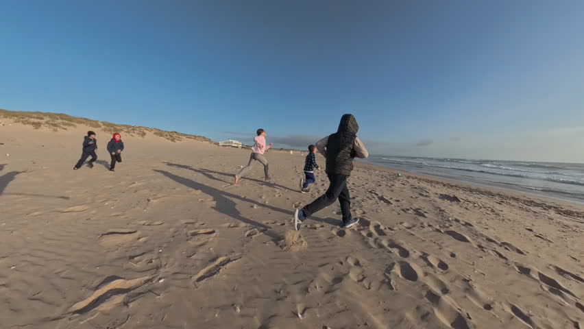 Little girl playing soccer barefoot on the beach with family