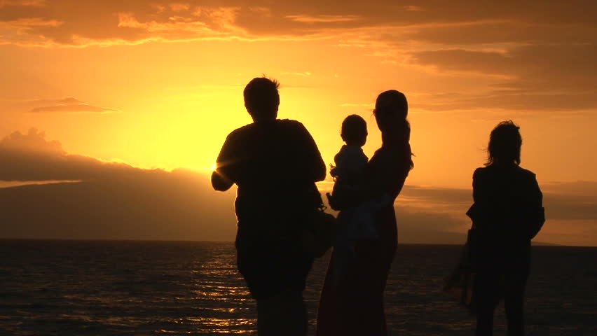 Silhouetted family with baby watching and taking photos of beautiful sunset.