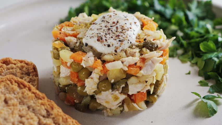Salad with beef, boiled potatoes, vegetables, and canned peas dressed with a creamy sauce. Classic Olivier salad.